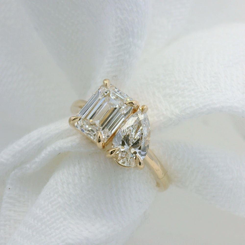 Diamond ring with emerald-cut and pear-shaped stones on a white fabric background