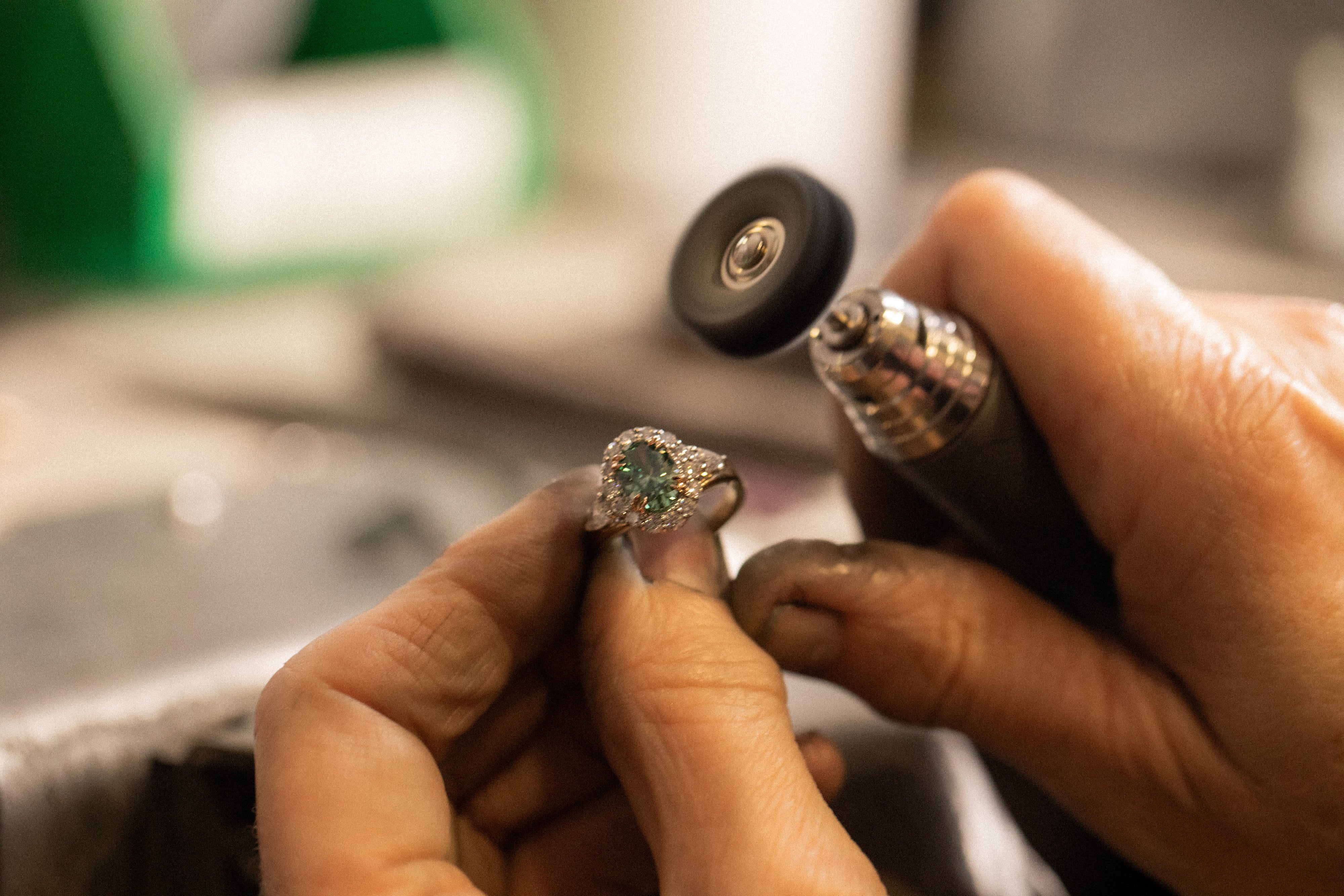 Person examining a ring with a green gemstone using a magnifying tool.