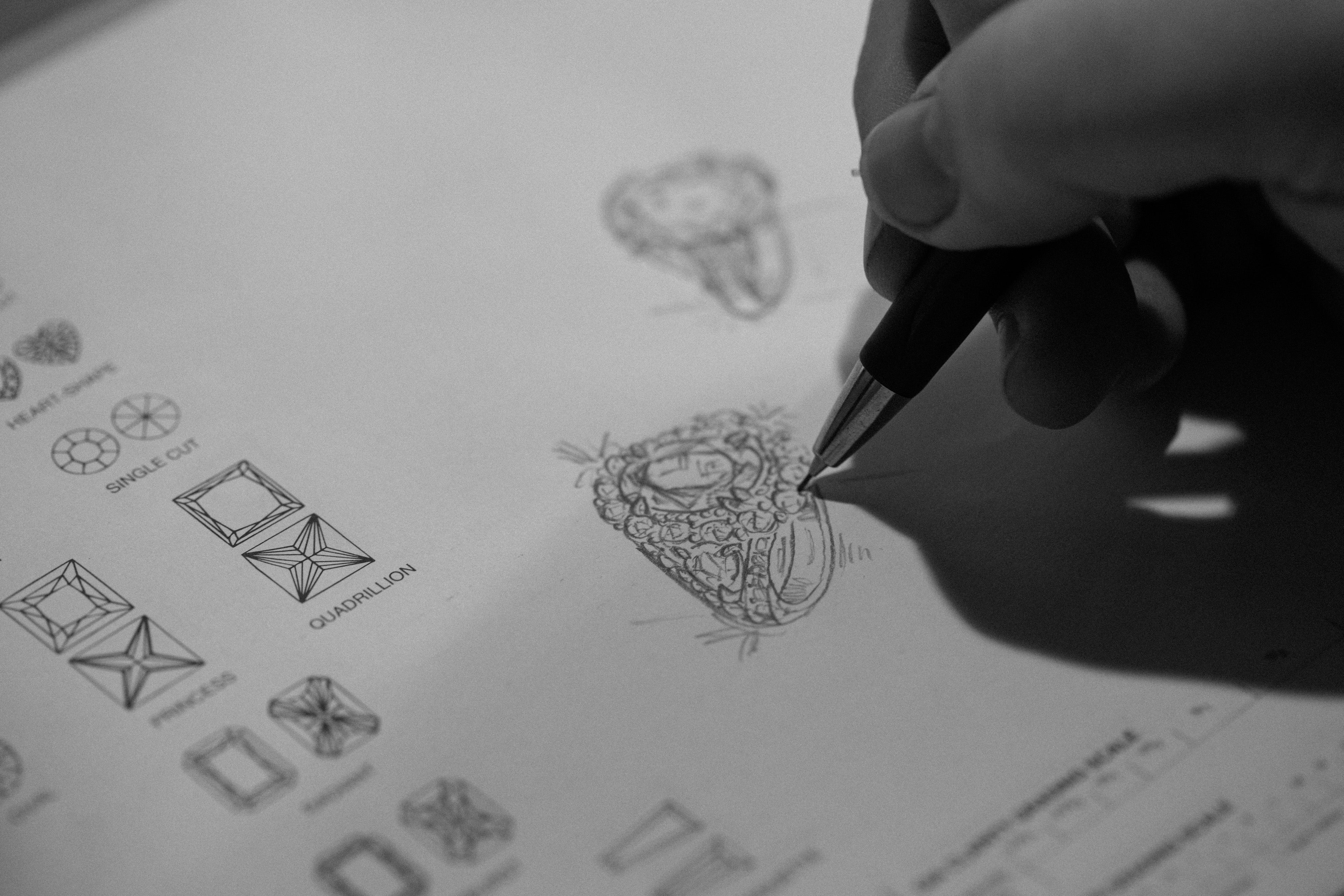 Hand drawing a diamond illustration on a sheet with various design sketches.