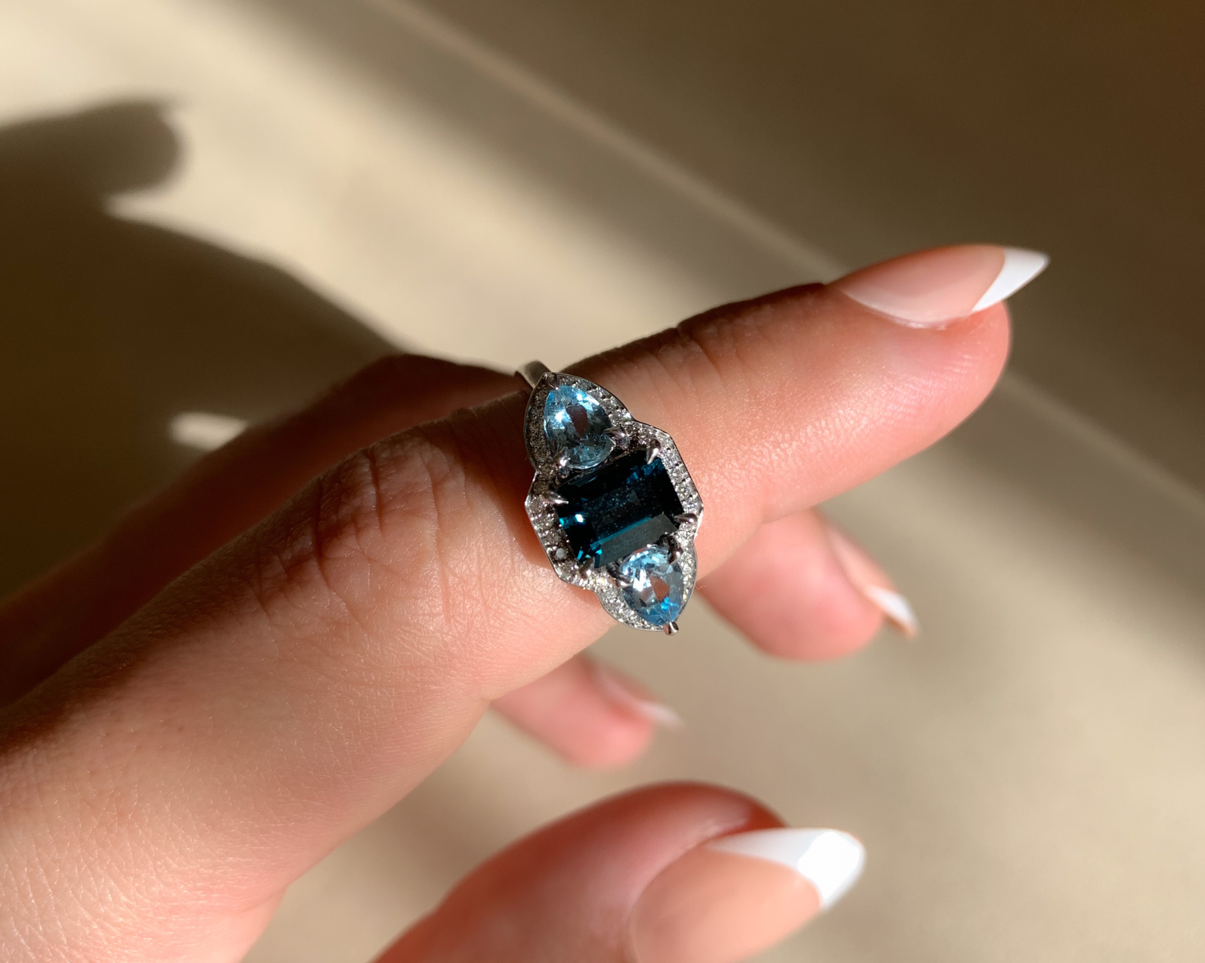 Hand wearing a ring with a blue gemstone against a neutral background