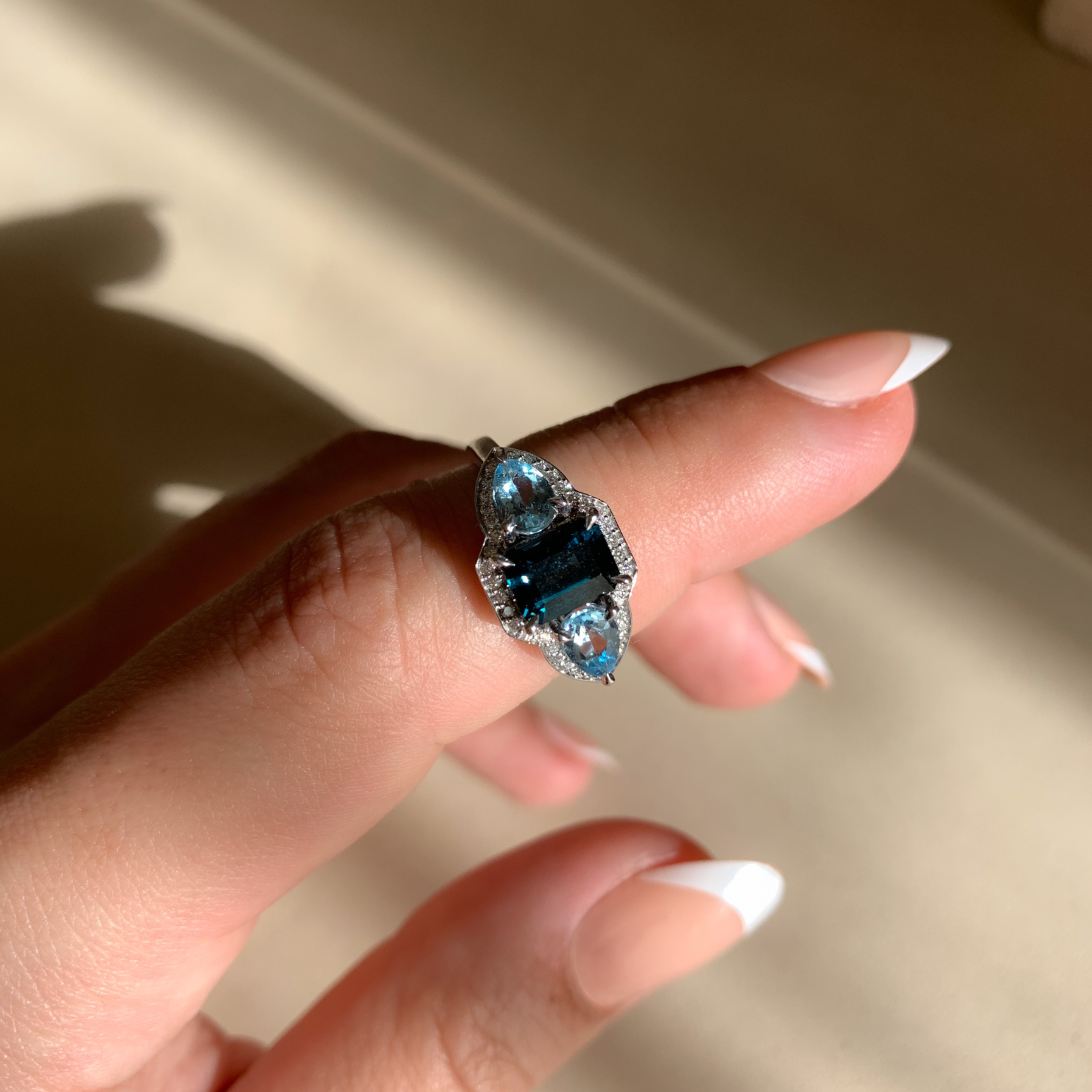 Hand wearing a ring with a blue gemstone against a neutral background
