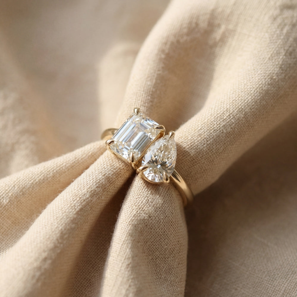Gold ring with emerald-cut and pear-shaped diamonds on beige fabric