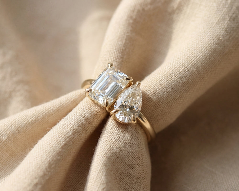 Gold ring with emerald-cut and pear-shaped diamonds on beige fabric