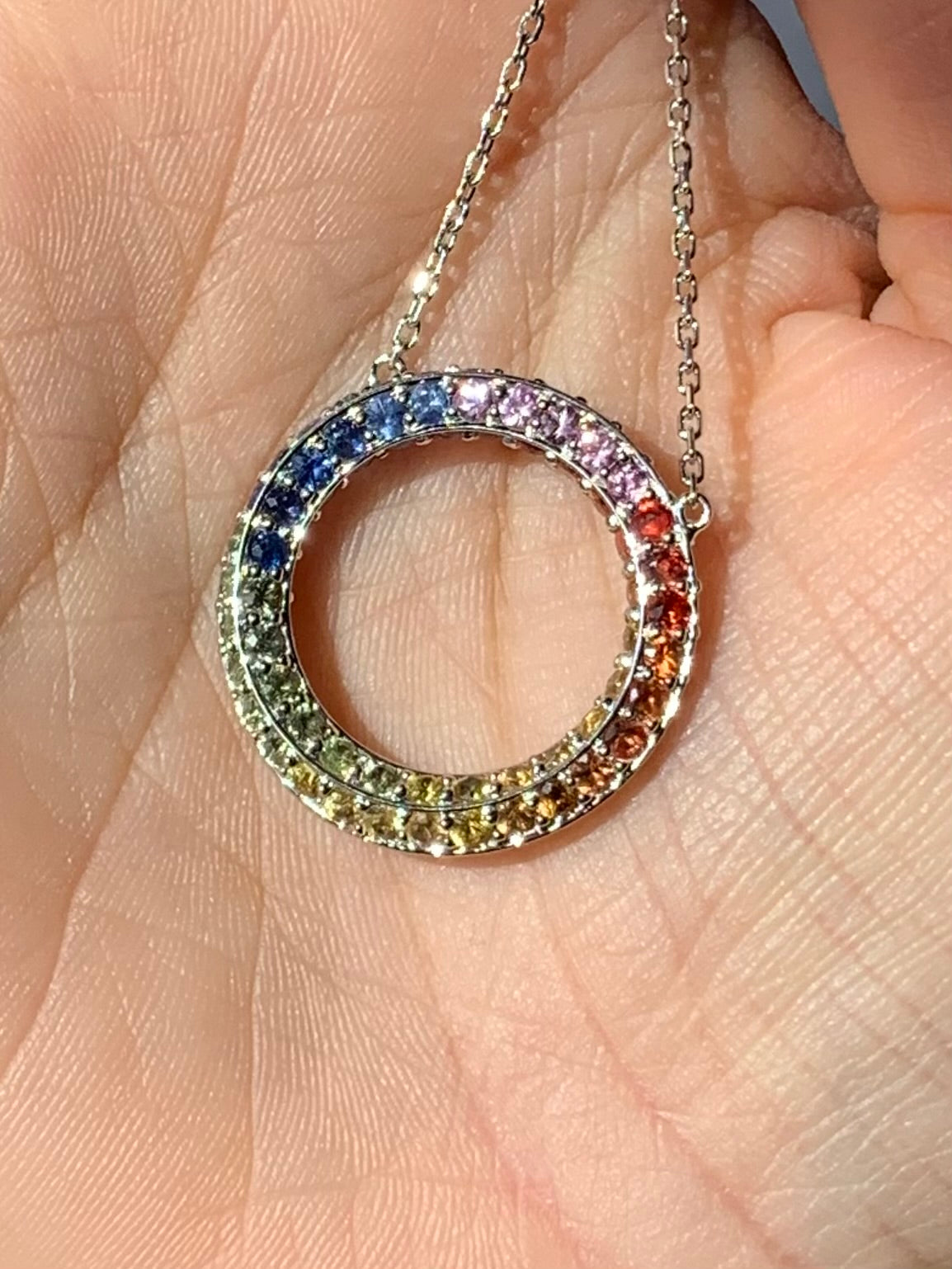Multicolored gemstone circle pendant on a chain held in hand