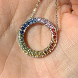 Multicolored gemstone circle pendant on a chain held in hand