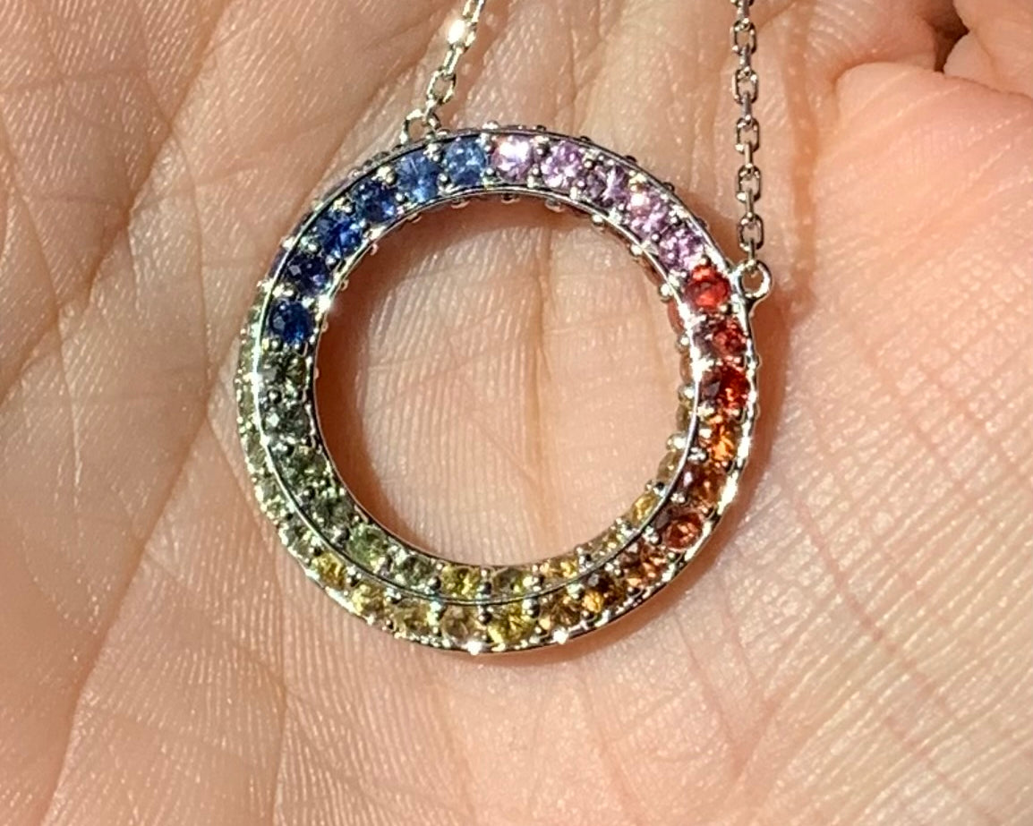 Multicolored gemstone circle pendant on a chain held in hand